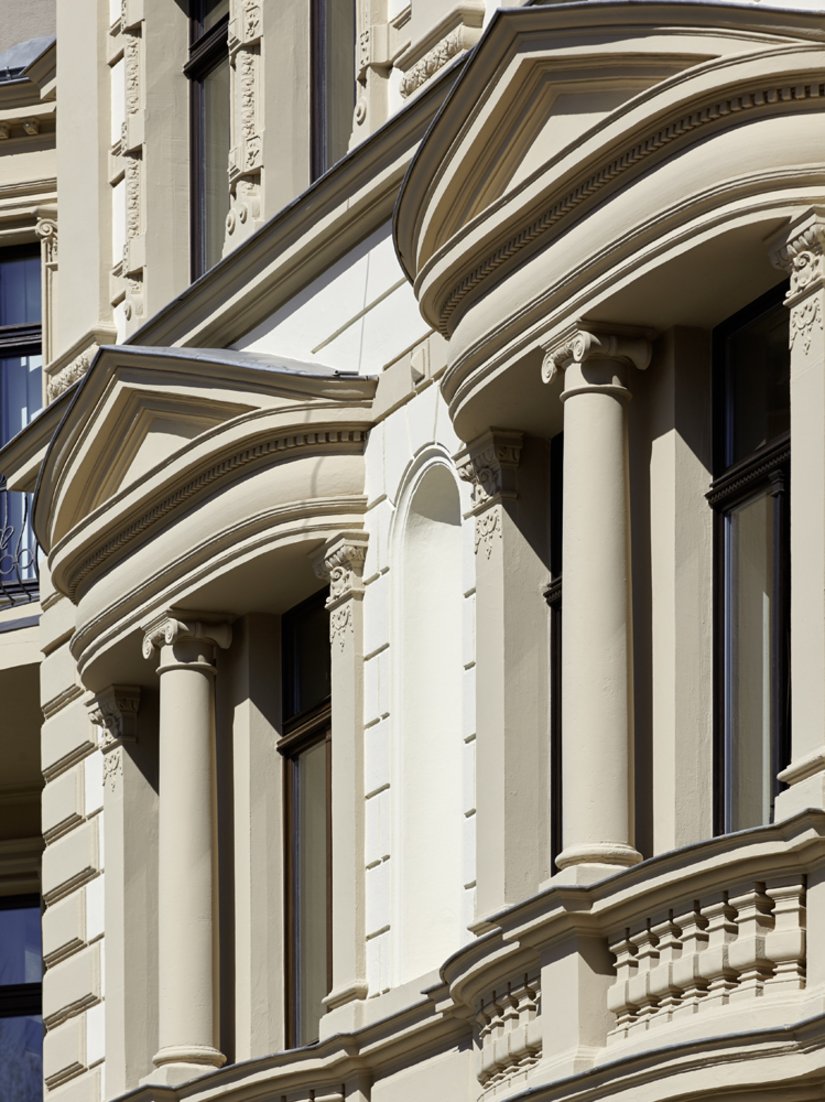 Sehr schön ist hier der Historismus typische Stilmix erkennbar. Die aufwendig plastisch mit Säulen, Balusterbrüstungen und Rundungen herausgearbeiteten Fenster des 1. OG ziehen die Aufmerksamkeit auf sich.