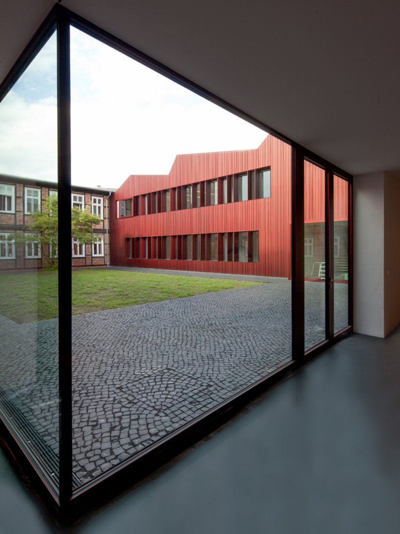 Eine alles überziehende Hülle aus rot eloxiertem Aluminiumblech kennzeichnet die Neubauten.