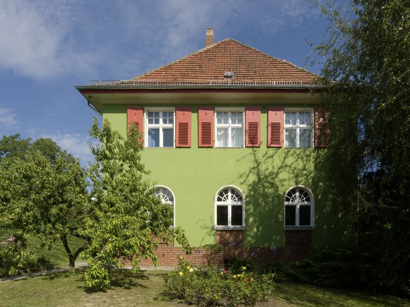 Das Grün bildet eine Leinwand für das Rot der Schlagläden, wobei sich das Gebäude harmonisch in die Natur einfügt.