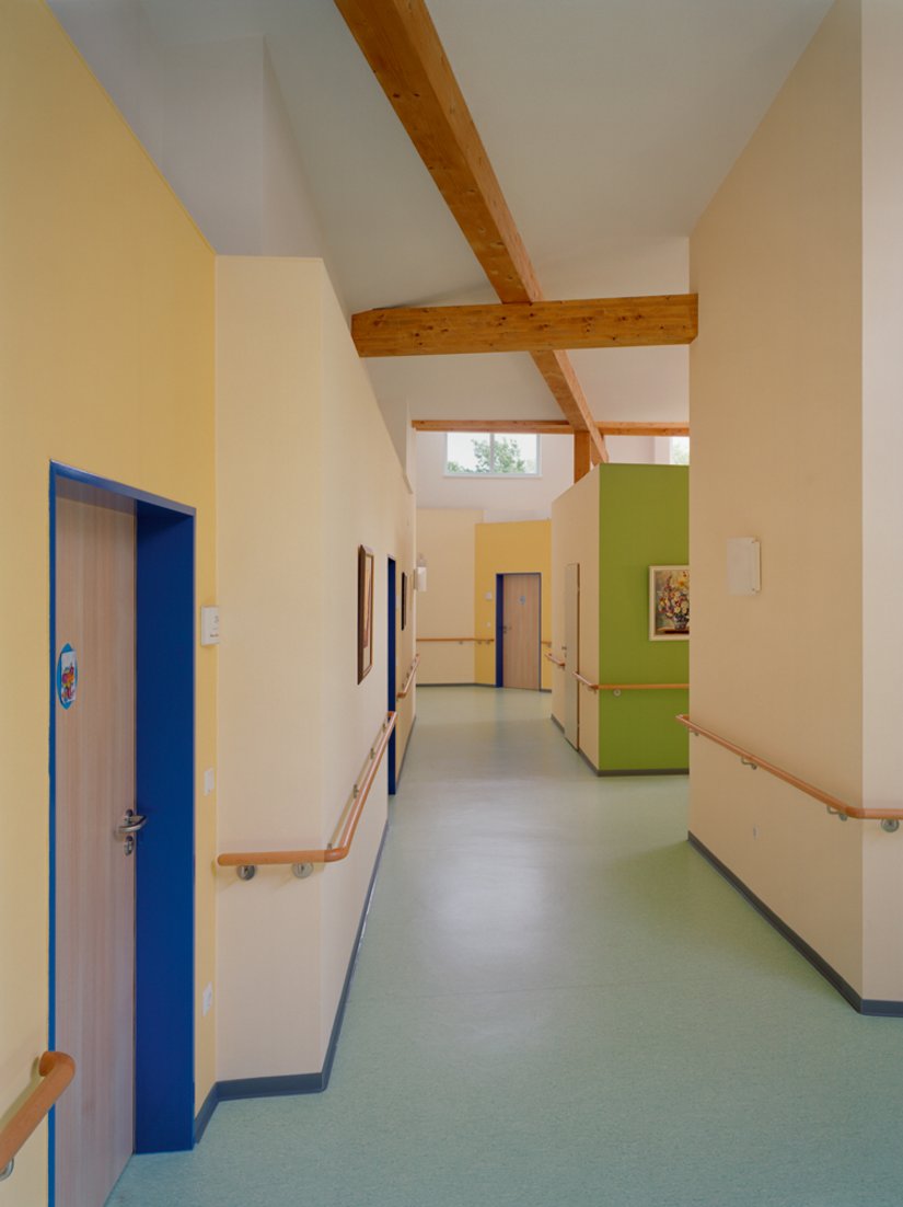 Schon von fern markiert ein als Putzmittelraum genutzter Raumwürfel in der Wohngruppen-Leitfarbe den Eingang zum Gemeinschaftszimmer. Der Kubus wird als Galeriefläche genutzt.