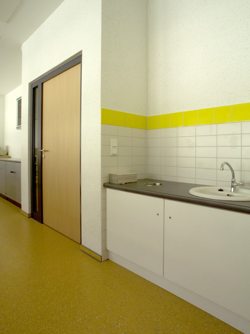 Sanitärräume müssen hygienisch sein, doch dies muss nicht immer mit dem sterilen Weiß gleichgesetzt werden. Das Gelb der Fensterrahmen wiederholt sich an den Fliesenspiegeln im Küchen- und Sanitärbereich.
