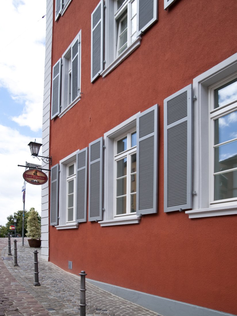 Graue Läden und weiße Fenster gliedern die rote Fassade.