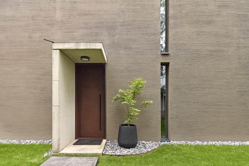 Die dunklen Holzfenster nehmen sich gestalterisch sehr zurück, während die massive Haustür aus Cortenstahl ein klares Statement setzt