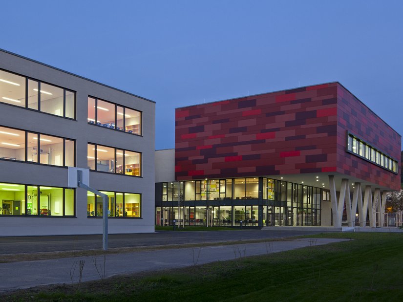 Prägnant ist die in vier Rot-Tönen changierende Faserzementfassade der Turnhalle im zweiten Obergeschoss.