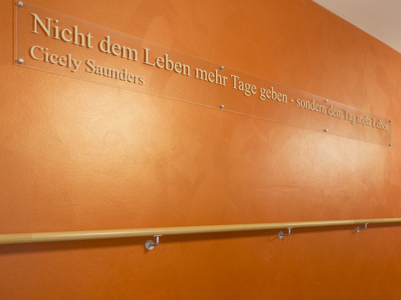 Im Flurbereich gibt ein kräftiges Orange in einer Gestaltungstechnik mit Creativ Lucento 83 den Ton an und sorgt mit dem auf die Wand applizierten Sinnspruch für eine aufheiternde Stimmung.
