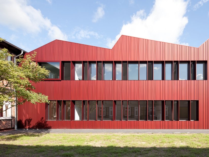 Die rötlich eloxierte Aluminiumfassade orientiert sich an der Farbigkeit der Bestandsbauten.