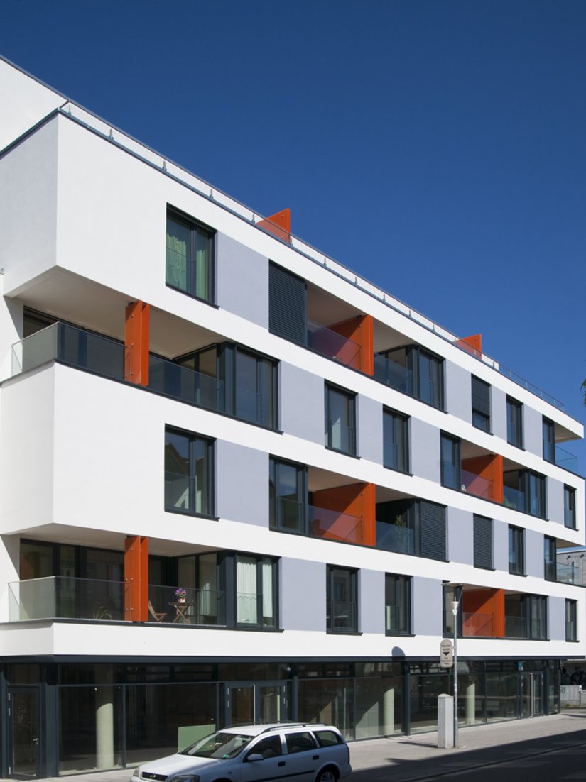 Die wärmegedämmte Fassade spielt mit ihren Fensteröffnungen und den Nischen der Loggien, die die Wirkung der Fassade bestimmen. Das Orangerot setzt Akzente, ohne die Wirkung des weißen Mäanders zu stören.