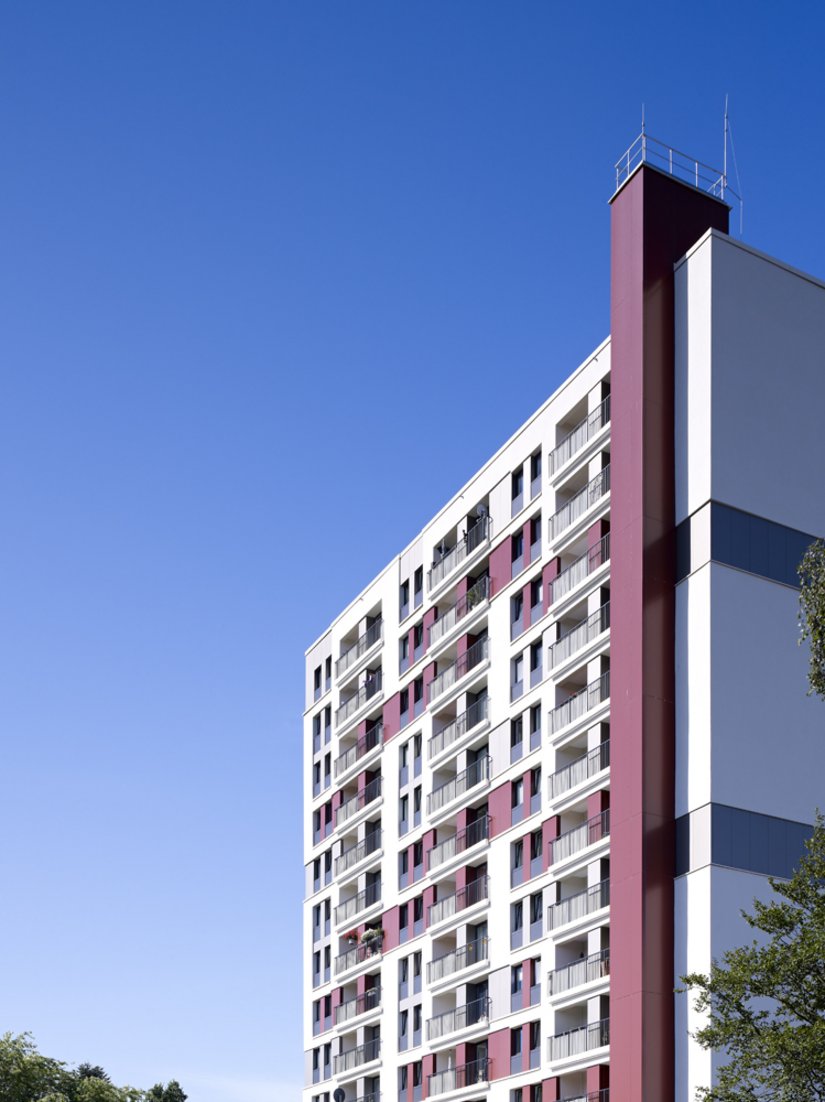 Ein plastisches Fassadenrelief in Sand-, Rot-, Grau- und Schwarztönen überlagert die Vertikalstruktur der Bestandsfassaden.