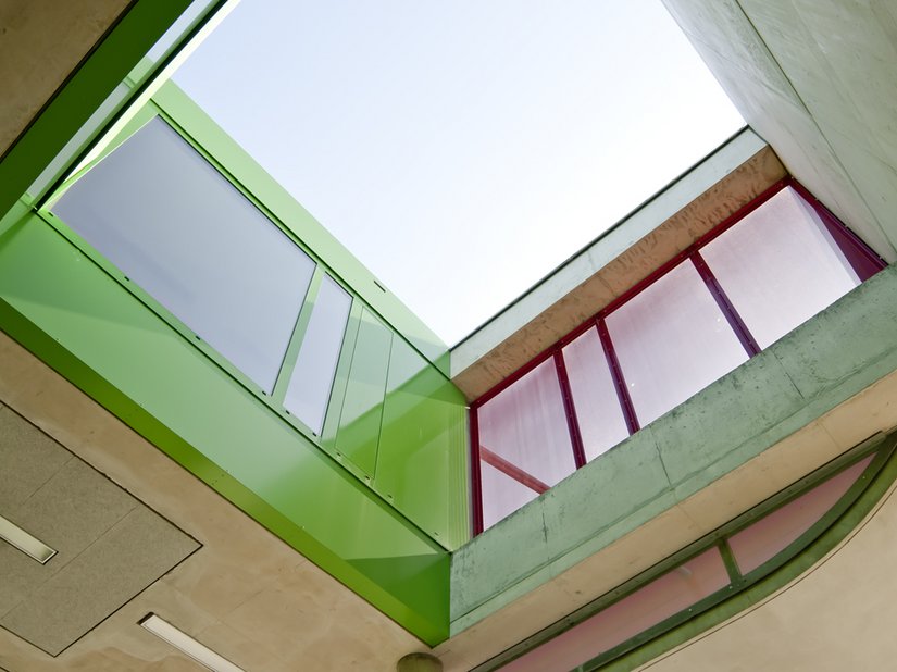 Die Lichthöfe im Inneren sind als grün lackierte metallene „Futterale“ ausgebildet. Die Betonoberflächen der Einschnitte der Außenräume sind dagegen betont rau strukturiert und partiell durch den vierlagigen Auftrag einer roten Lasur akzentuiert.