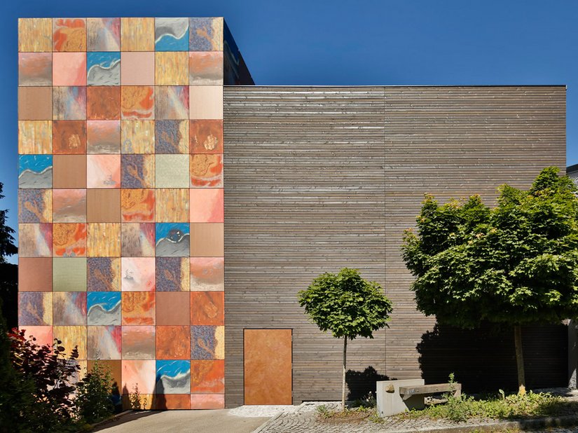 Das Gebäude entwickelt mit der extravaganten Fassadengestaltung seines farbigen Turms aus Alucobondplatten in warmen Rot-, Braun und Blautönen und integrierten Künstlerporträts eine enorme Strahlkraft.