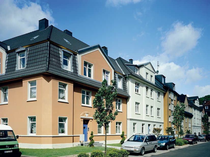 Bei dem erdroten Eckgebäude ist das Dach tiefer gezogen, so dass die Fassade einen kräftigen Farbton braucht um die Massivität der Dachfläche aufzufangen. Die im Straßenverlauf folgenden Häuser sind im Wechsel und im Bezug auf die Bauweise gestaltet. Moderner Hingucker sind die Türen in sattem Blau.