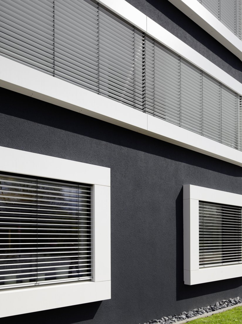 Die plastisch betonte, weiße Umrahmung der horizontalen Fensterbänder integriert den außenliegenden Sonnenschutz und den notwendigen, horizontalen Fensterschluss in die Fassadenkonstruktion.